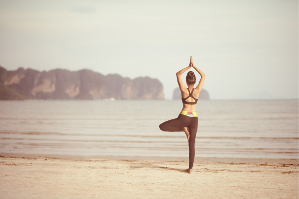 Mujer practicando yoga barefoot en la playa, con excelente postura y conexión con la tierra, base para la alineación corporal.